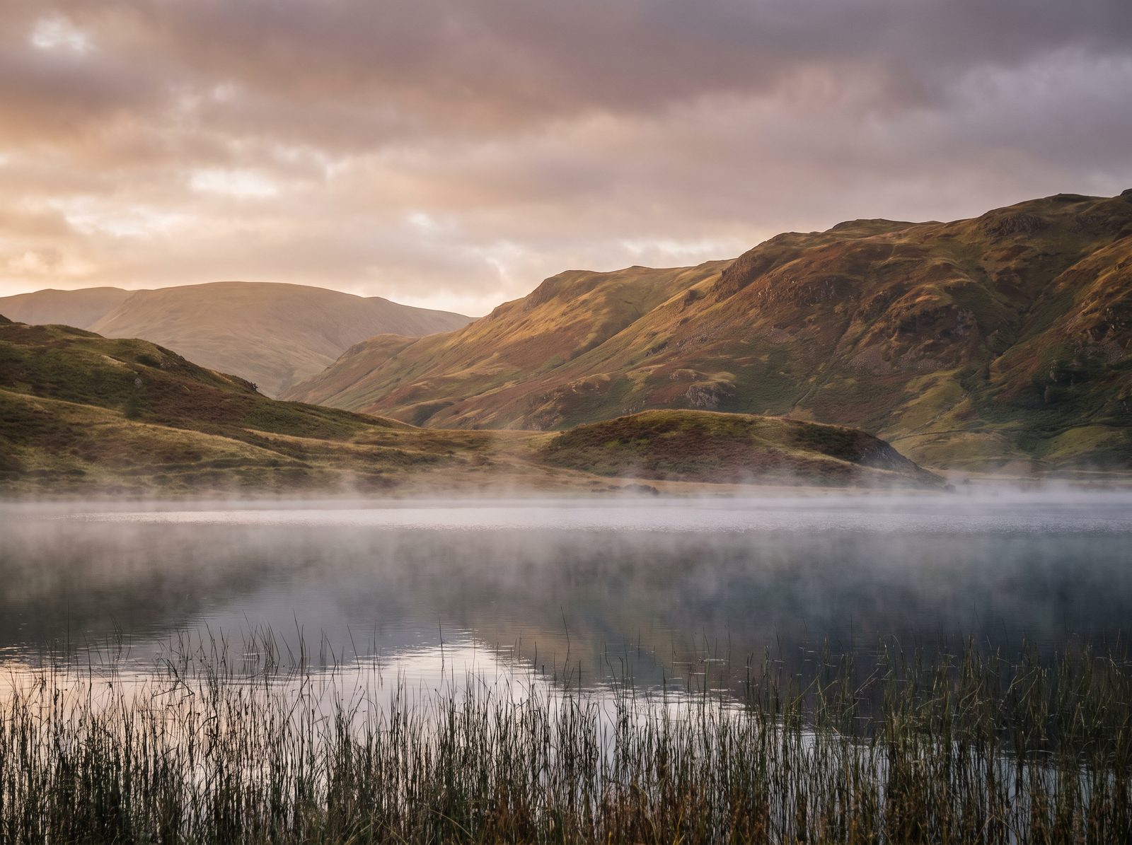 Morning mist over a still lake with hills behind