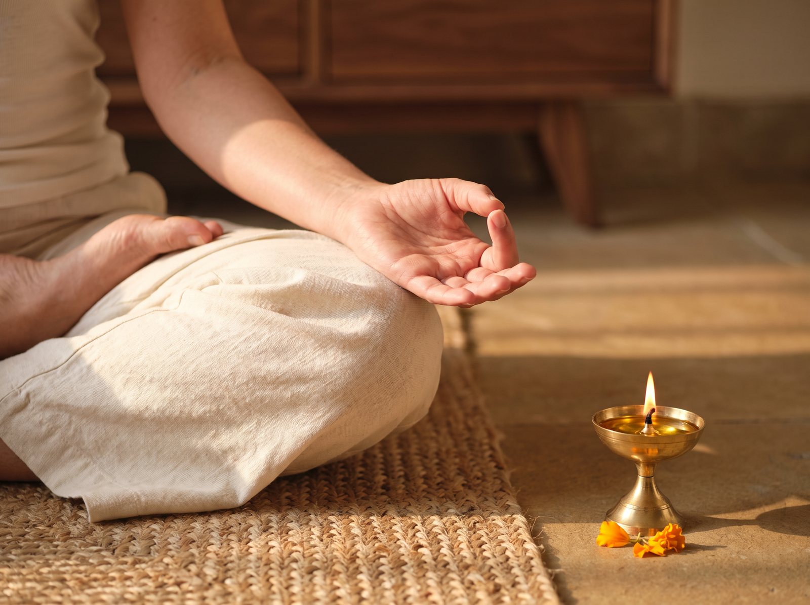 A hand resting on the knee in a meditation gesture beside a lit brass lamp